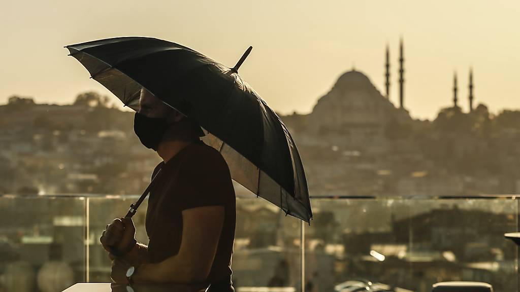 ARCHIV - Ein Tourist trägt einen Mund-Nasen-Schutz und hält einen Regenschirm während er von der Süleymaniye-Moschee über die Stadt blickt. (Archivbild) Foto: Emrah Gurel/AP/dpa