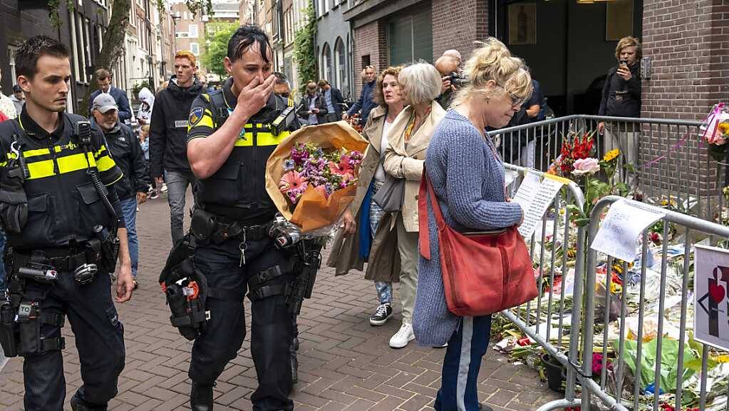 Polizisten bringen einen Blumenstrauss zu dem Blumenmeer für den Reporter Peter R. de Vries.