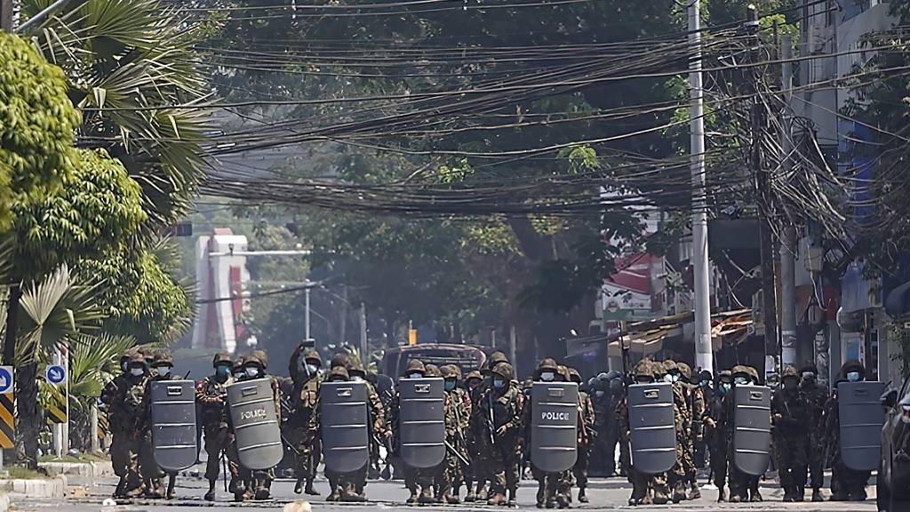 Einsatzkräfte des Militärs mit Schutzschilden bewegen sich während eines Protests in Rangun eine Straße hinauf. Foto: Uncredited/AP/dpa