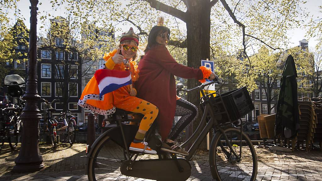 Eine Mutter und ihre Tochter, die ein orangefarbenes Königsgewand mit der niederländischen Flagge trägt, am Königstag in Amsterdam. Foto: Peter Dejong/AP/dpa