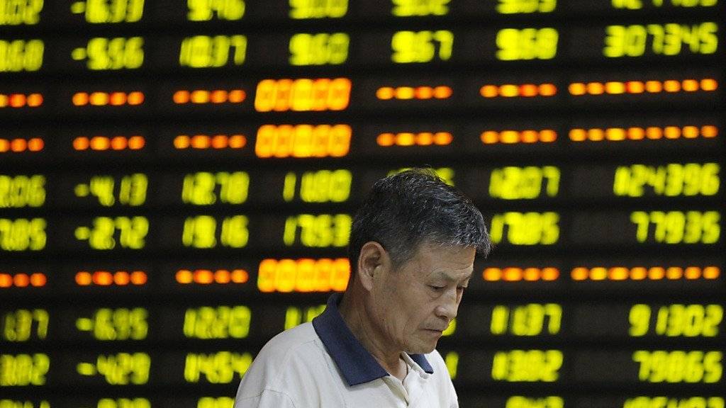 Ein Chinese steht niedergeschlagen vor einer Digitalanzeige mit Börsendaten - die chinesische Regierung will nach dem Taucher der Börse mit Stützkäufen eingreifen. (Symbolbild)