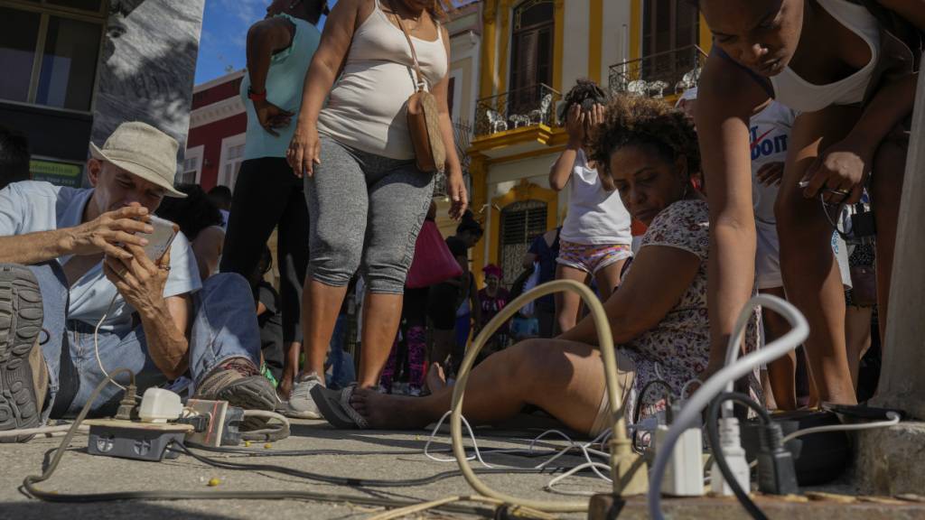 ARCHIV - Anwohner laden ihre elektronischen Geräte auf einer Straße während eines Stromausfalls in Havanna. Foto: Ramon Espinosa/AP/dpa