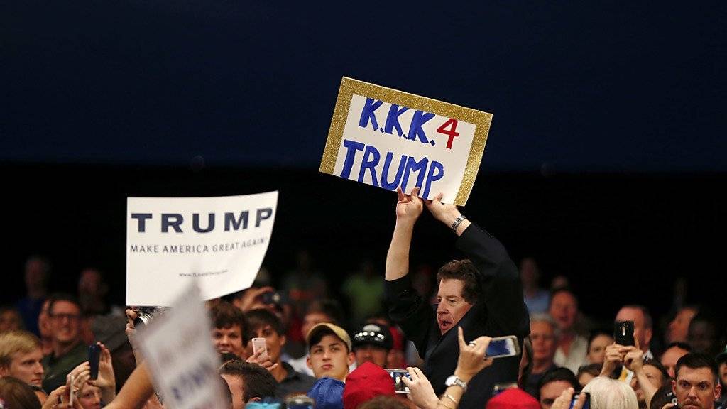Ein Mann hält in New Orleans während einer Wahlkampfveranstaltung Trumps ein Plakat hoch, auf welchem er ihn mit dem rassistischen Ku-Klux-Klan in Verbindung bringt
