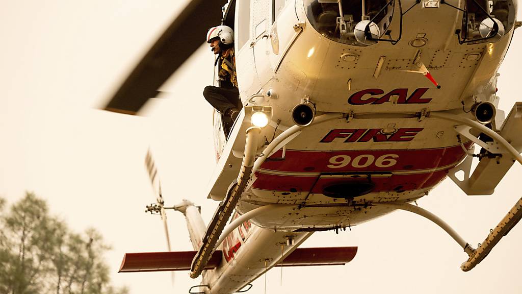 Ein Feuerwehrmann schaut aus einem Hubschrauber heraus, während er an den Löscharbeiten eines Waldbrandes beteiligt ist. Foto: Noah Berger/AP/dpa