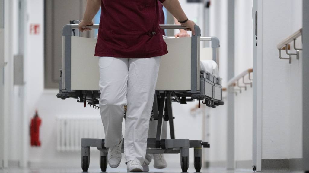 Eine Krankenpflegerin und ein Krankenpfleger schieben ein Krankenbett durch den Gang einer Station eines Krankenhauses. +++ dpa-Bildfunk +++