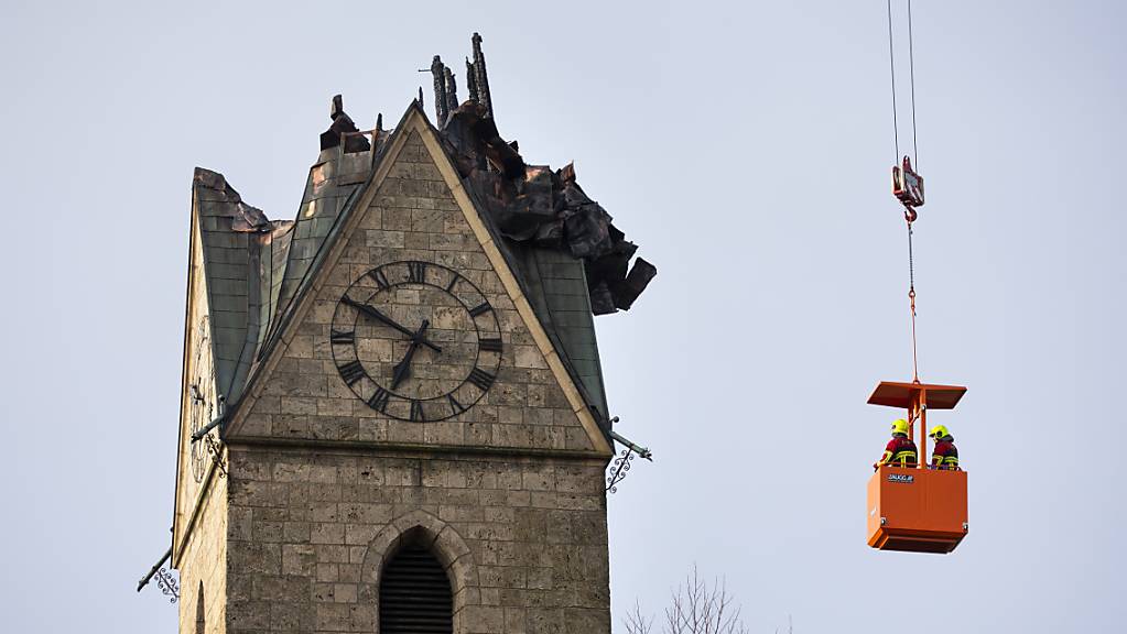 Feuerwehrleute schauen sich die abgebrannte Spitze des Kirchturms in Herzogenbuchsee BE an. Der Sachschaden wird auf mehrere Millionen Franken geschätzt.
