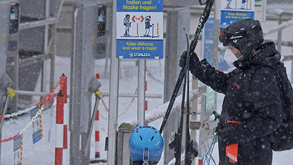 Skifahrer stehen vor einer Corona-Schleuse mit den Hinweisen, Abstand zu halten und eine Maske zu tragen, an einem Skilift im Skigebiet «Stuhleck» am Semmering in Niederösterreich. Foto: Herbert Pfarrhofer/APA/dpa