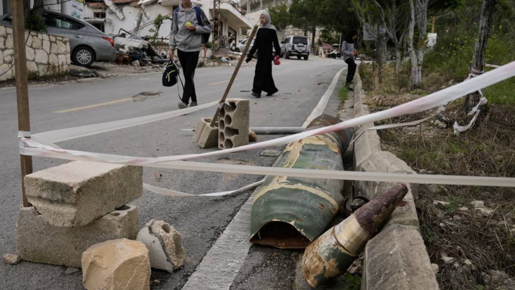 Menschen gehen neben Raketenteilen im Dorf Halloussiyeh im Südlibanon vorbei. Foto: Bilal Hussein/AP/dpa