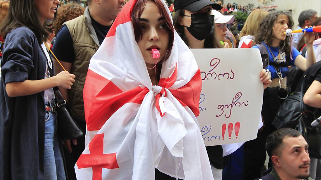 Ein in eine georgische Nationalfahne gehüllte Demonstrantin steht während einer Protestaktion der Opposition gegen das Gesetz über ausländische Einflussnahme vor dem Parlamentsgebäude vor der Polizei. Foto: Shakh Aivazov/AP/dpa
