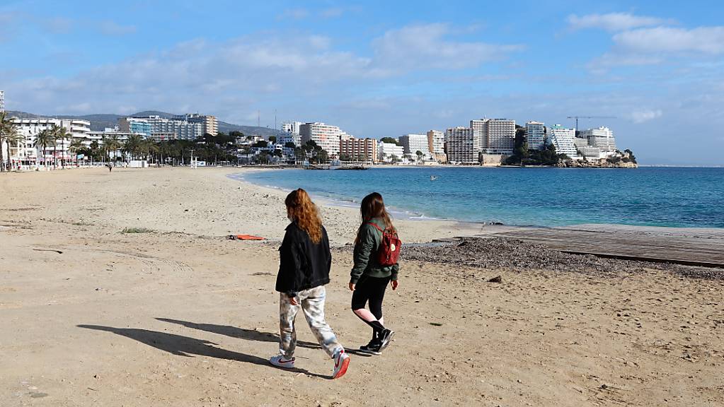 Zwei junge Frauen gehen am leeren Strand von Magaluf entlang.