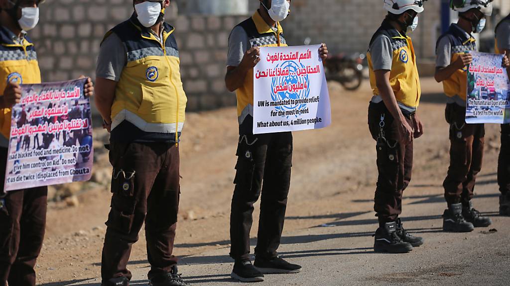 Mitglieder des Syrischen Zivilschutzes (Weißhelme) halten Schilder mit Aufschriften und nehmen an einem Protest auf der Autobahn in Richtung des Grenzübergangs Bab Al-Hawa teil, um die Verlängerung des Einreisemandats für humanitäre Helfer in den Nordwesten Syriens zu fordern. Foto: Anas Alkharboutli/dpa