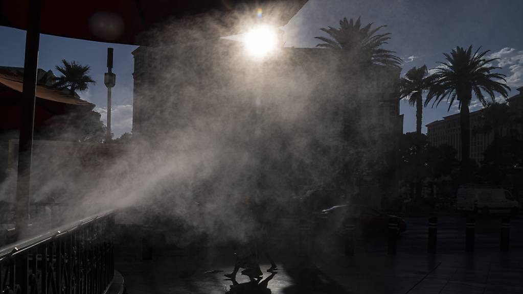dpatopbilder - Menschen gehen in Las Vegas an Nebelmaschinen vorbei, die zur Abkühlung entlang des Las Vegas Strip eingesetzt werden. Las Vegas könnte an diesem Wochenende sein Temperatur-Allzeithoch erreichen, da für den Bundesstaat und große Teile der westlichen USA extreme Hitze vorhergesagt wird. Foto: John Locher/AP/dpa