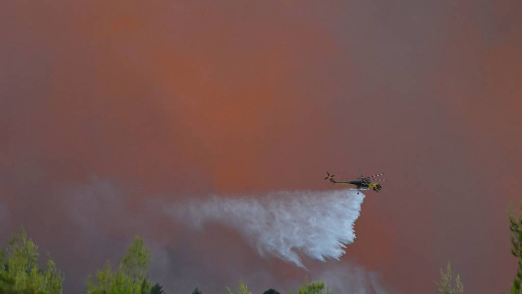 dpatopbilder - Ein Hubschrauber wirft nordwestlich von Athen während der Waldbrände Löschmittel ab. Foto: Michael Varaklas/AP/dpa