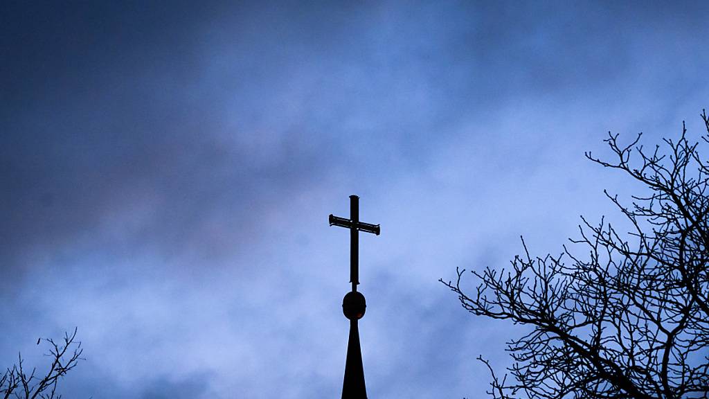 PRODUKTION - Dunkle Wolken ziehen über das Kreuz auf einer evangelischen Kirche in Niedersachsen hinweg.. Foto: Julian Stratenschulte/dpa