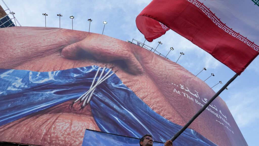 ARCHIV - Ein Mann schwenkt in Teheran eine iranische Flagge vor einer Plakatwand mit einer Darstellung der Straße von Hormus und zugenähten Lippen von US-Präsident Trump. Foto: Vahid Salemi/AP/dpa/Archivbild