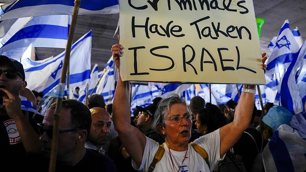 Eine Demonstrantin hält ein Plakat mit der Aufschrift «Criminals have taken Israel» während einer Demonstration am Flughafen Ben Gurion. Foto: Ariel Schalit/AP/dpa