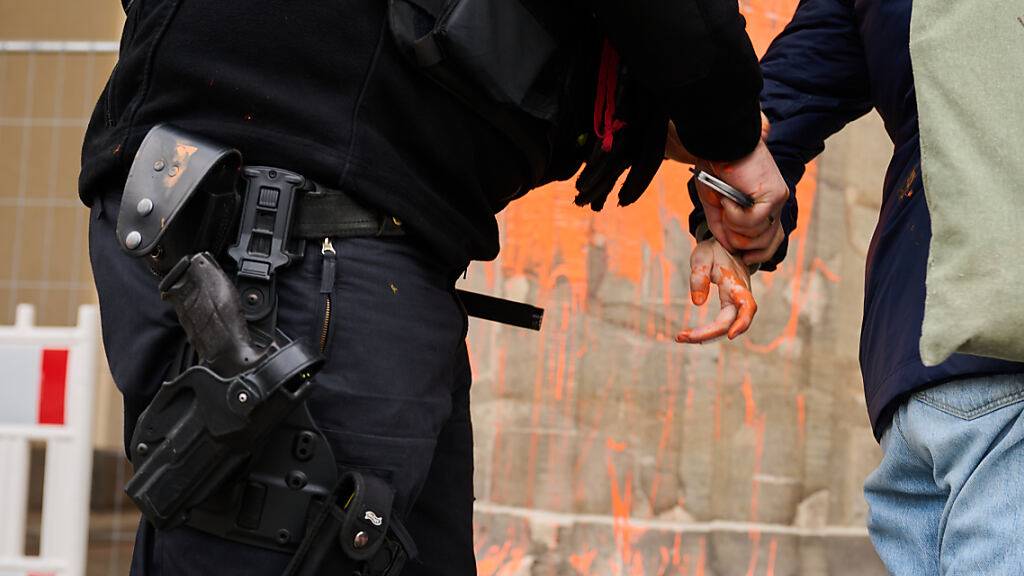 Ein Polizeibeamter (l) nimmt eine Klimaaktivistin in Gewahrsam, die das Brandenburger Tor mit oranger Farbe bemalt hat. Foto: Annette Riedl/dpa
