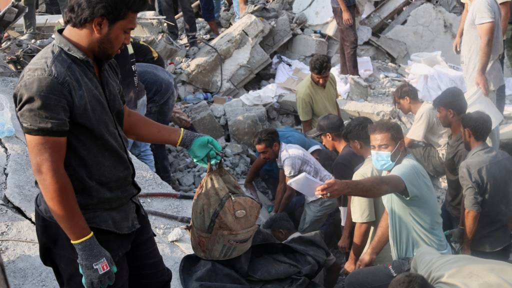 Ein Mann hält einen Kinderrucksack, während Rettungskräfte und Anwohner die Trümmer nach einem israelisch-amerikanischen Angriff auf eine Mädchengrundschule durchsuchen. Foto: Uncredited/Mehr News Agency/AP/dpa