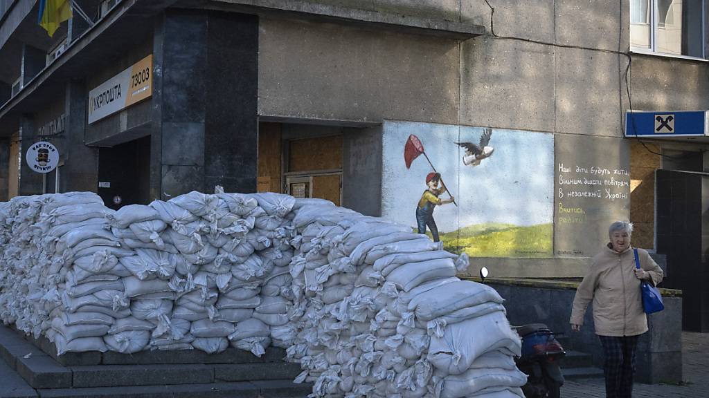 Ein Anwohner geht an Sandsäcken vorbei, die das Postamt der Stadt schützen, rund ein Jahr, nachdem ukrainische Einheiten die Stadt befreit und russische Truppen vertrieben hatten. Foto: Efrem Lukatsky/AP/dpa