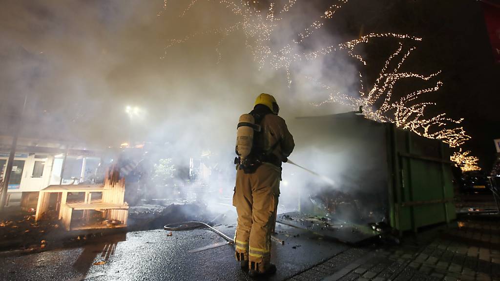 Krawalle in Rotterdam: Ein Feuerwehrmann löscht einen Container, der bei Protesten gegen eine landesweite Ausgangssperre in Brand gesetzt wurde. Foto: Peter Dejong/AP/dpa