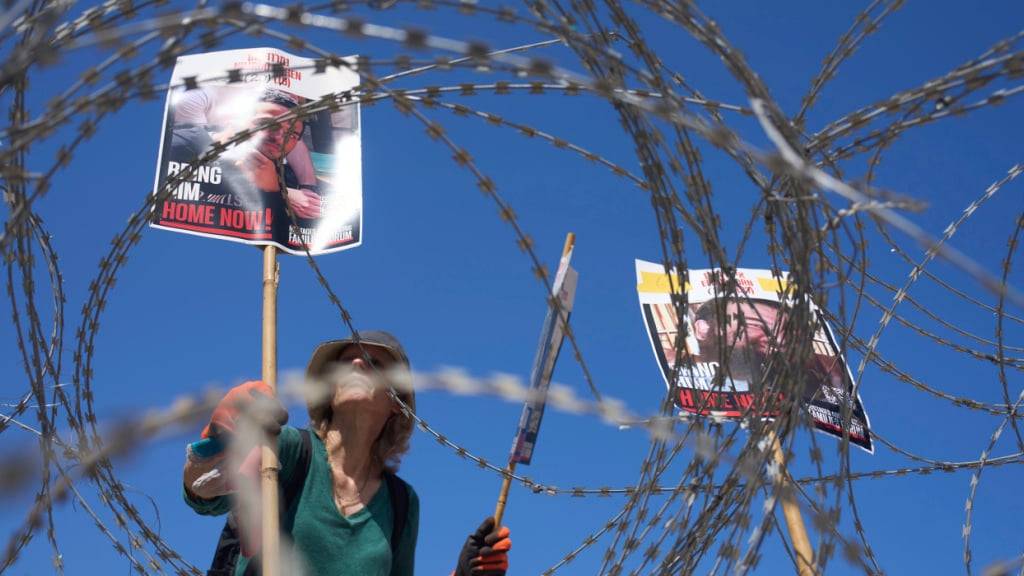dpatopbilder - Eine Frau platziert Bilder der Geiseln Nimrod Cohen (l) und Eitan Horn, die von der Hamas im Gazastreifen gefangen gehalten werden, auf einem Stacheldraht während eines Protestes von Familien auf dem Platz der Geiseln. Foto: Ariel Schalit/AP/dpa