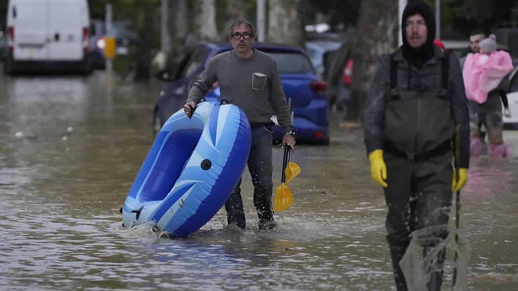 Menschen bahnen sich ihren Weg auf einer überfluteten Straße in der mittelitalienischen Region Toskana. Foto: Gregorio Borgia/AP/dpa