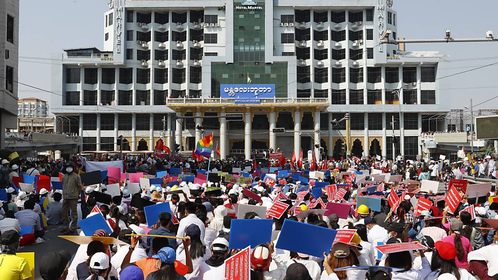 Teilnehmer eines Protestes gegen den jüngsten Militärputsch versammeln sich mit Plakaten vor dem Bahnhofsgebäude. Myanmars entmachtete Regierungschefin Suu Kyi bleibt zunächst weiter in Gewahrsam. Foto: Uncredited/AP/dpa