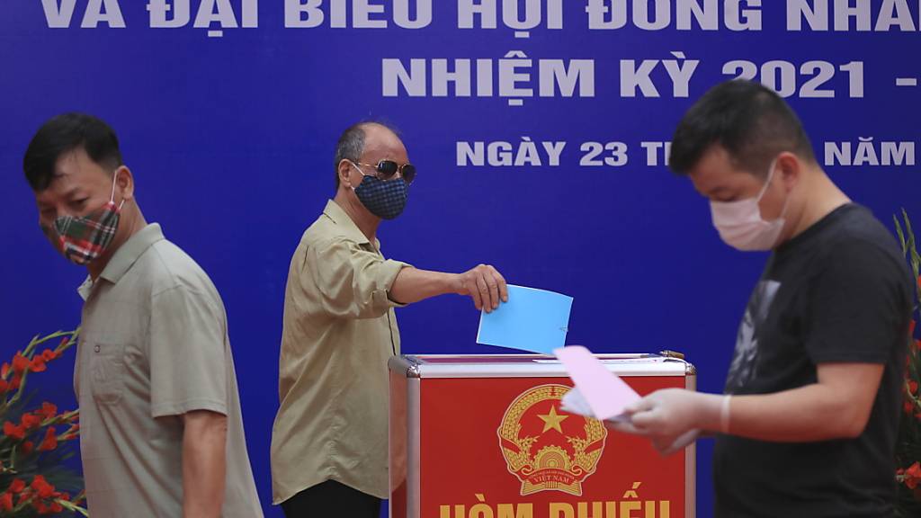 Menschen mit Mund-Nasen-Schutz stimmen bei der Wahl der Nationalversammlung in einem Wahllokal ab. Foto: Hau Dinh/AP/dpa