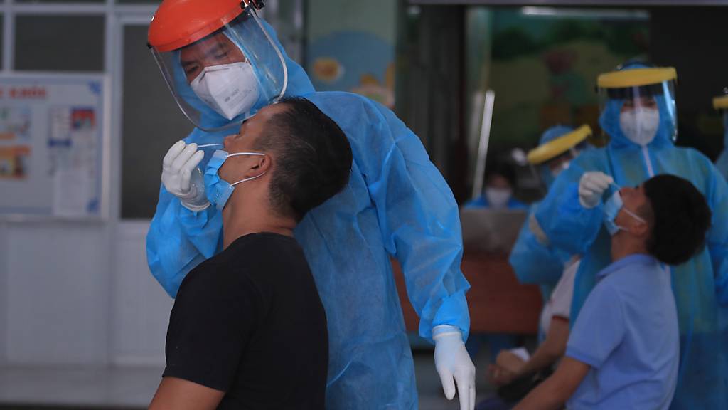 Mitarbeiter im Gesundheitswesen entnehmen zwei Männern einen Abstrich. Vietnam hat am Sonntag nach Angaben des Gesundheitsministeriums 737 Tote im Zusammenhang mit dem Coronavirus registriert - so viele Tote binnen eines Tages hat es in dem Land noch nie seit Beginn der Pandemie gegeben. Foto: Hau Dinh/AP/dpa