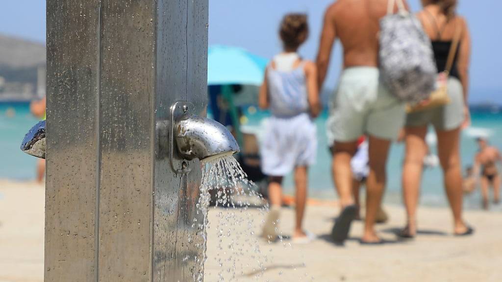 ARCHIV - Menschen gehen an einer Stranddusche am Playa de Muro vorbei. Foto: Clara Margais/dpa