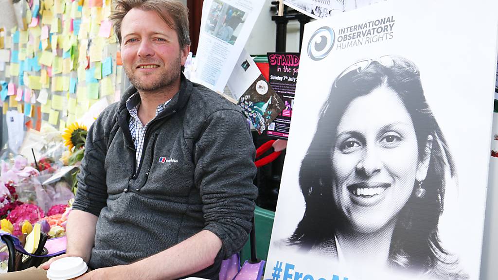 ARCHIV - Richard Ratcliffe, der Ehemann der im Iran inhaftierten Nazanin Zaghari-Ratcliffe, sitzt neben einem Bild seiner Frau vor der iranischen Botschaft in London. Foto: Jonathan Brady/PA Wire/dpa