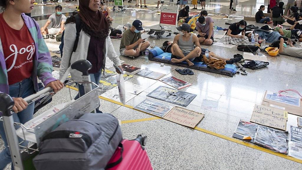 Passagiere gehen am Flughafen von Hongkong an Protestierenden vorbei.