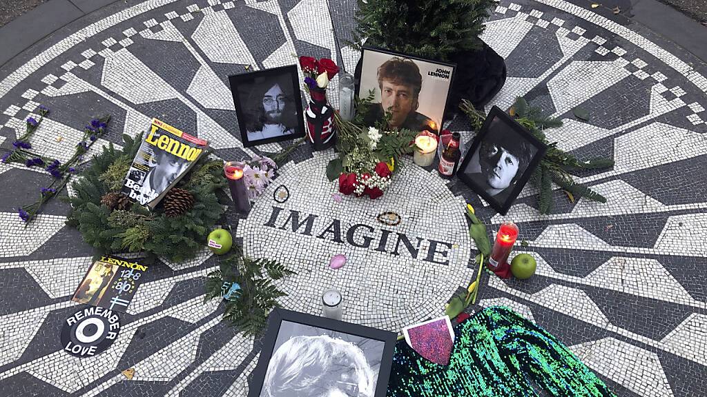 Fotos, Blumen und Kerzen stehen auf der Gedenkstätte Strawberry Fields im Central Park zur Erinnerung an John Lennon. Vor genau 40 Jahren wurde der Beatles-Musiker in New York erschossen. Der Mörder sitzt bis heute im Gefängnis. Foto: Mark Lennihan/AP/dpa