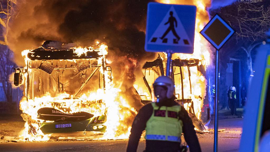 Bereitschaftspolizisten im schwedischen Malmö beobachten einen brennenden Stadtbus.