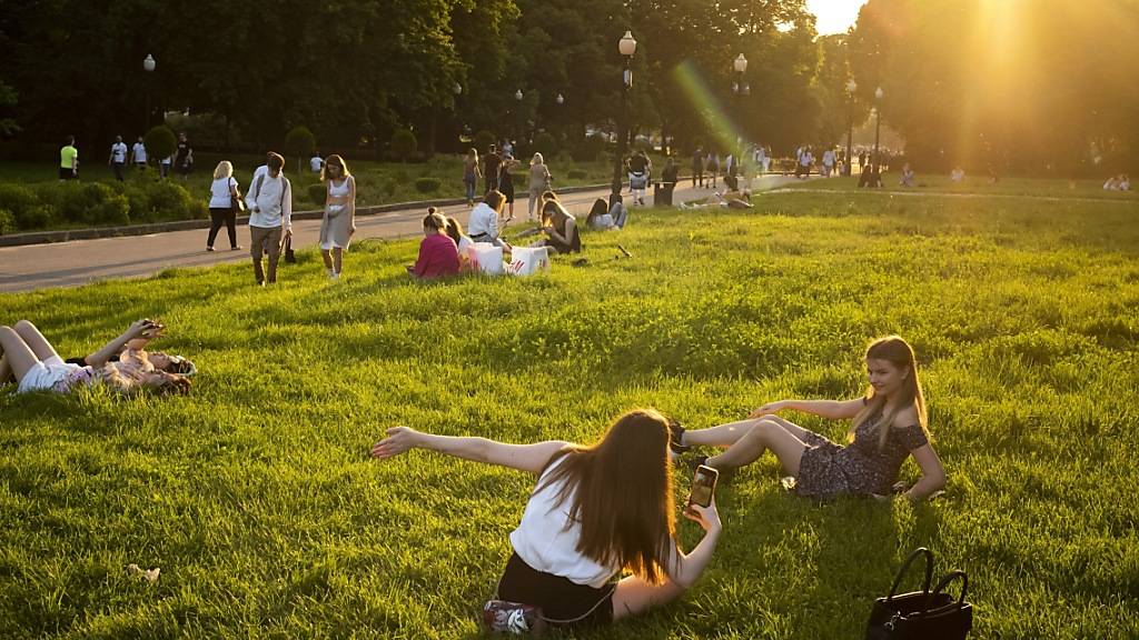 Menschen genießen das warme Wetter im Gorki-Park während des Sonnenuntergangs. Die Behörden in Moskau haben die Ende März wegen des Ausbruchs des Coronavirus eingeführten strengen Sperrmaßnahmen gelockert. Foto: Alexander Zemlianichenko/AP/dpa