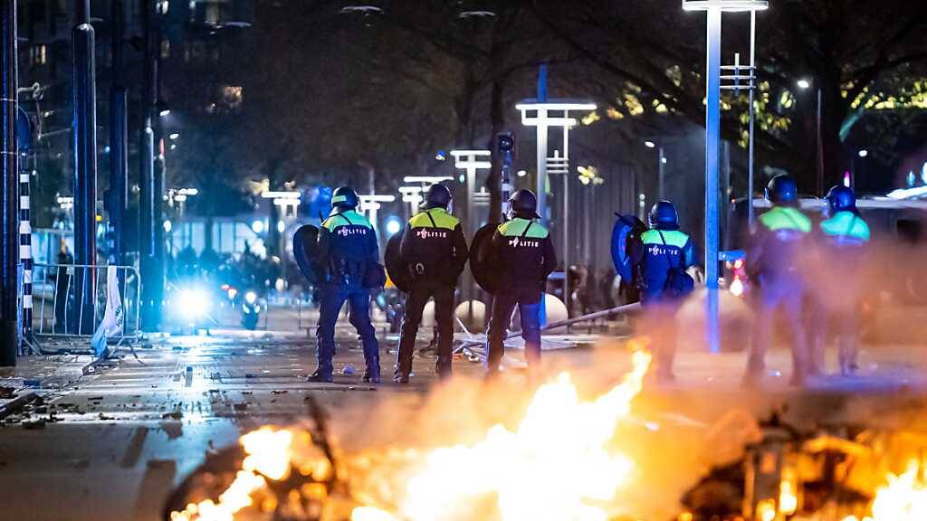 Polizisten stehen während Ausschreitungen auf einer Straße vor einem Feuer. Bei schweren Ausschreitungen in Rotterdam bei einer Kundgebung gegen schärfere Corona-Regeln hat es nach Schüssen der Polizei Verletzte gegeben. Foto: ---/ANP MEDIA-TV/dpa