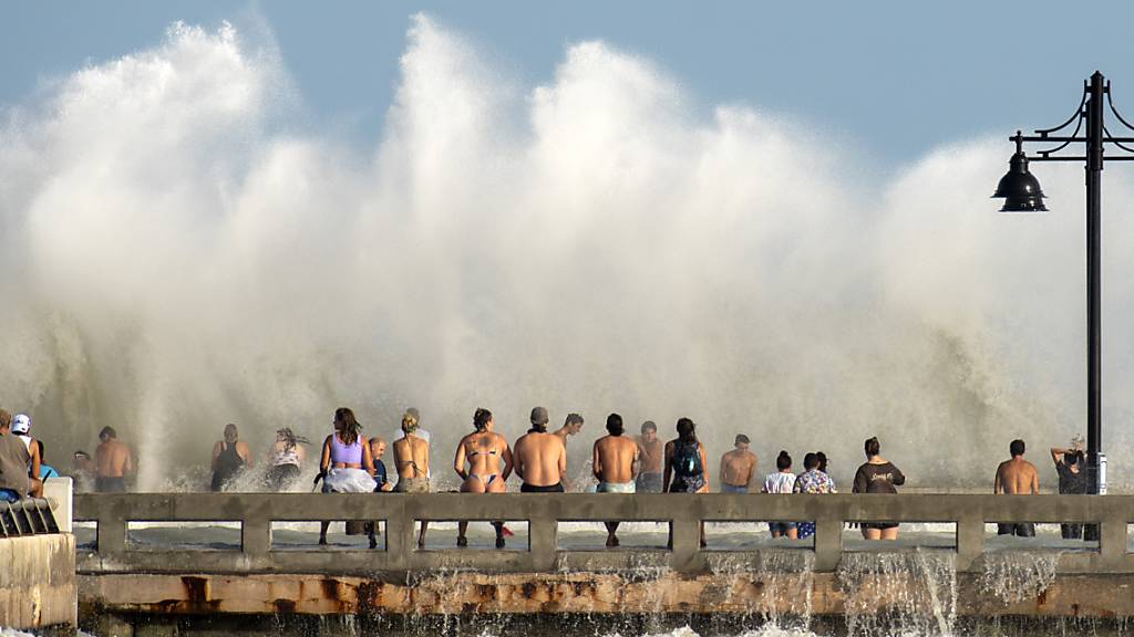 Strandbesucher stehen vor einer großen Welle, die wegen des starken Tropensturms «Laura» zustande kommt. Ungefähr 100 Anwohner kamen zum beliebten Pier, um sich den Wind und die großen Wellen anzusehen. Foto: Rob O'neal/The Key West Citizen/dpa