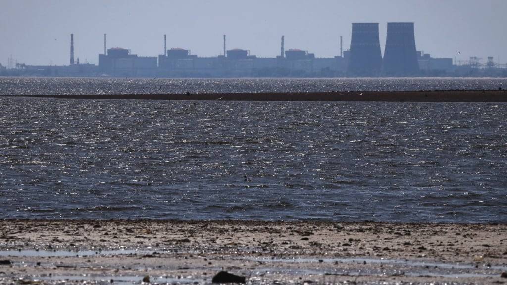 ARCHIV - Das Kernkraftwerk Saporischschja ist im Hintergrund des flachen Kachowka-Stausees nach der Zerstörung des Staudamms zu sehen. Das von russischen Truppen besetzte Atomkraftwerk Saporischschja ist wieder mit dem ukrainischen Stromnetz verbunden. Foto: Kateryna Klochko/AP/dpa