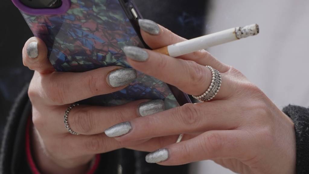 ARCHIV - Eine Frau raucht auf einer Straße, während sie in ihr Handy schaut. In Mailand ist das Rauchen im Freien künftig allenfalls mit zehn Metern Abstand erlaubt. Foto: Kin Cheung/AP/dpa