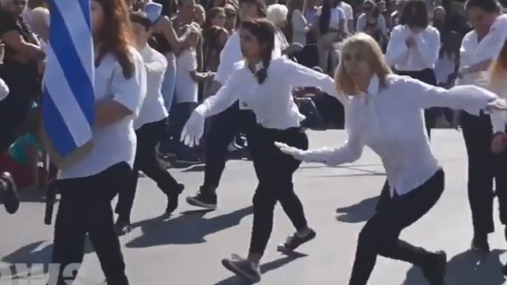 Videos zeigen, wie die zehn Mädchen aus Athen bei der Schüler- und Militärparade an verdutzten offiziellen und kirchlichen Würdenträgern vorbeiwackeln, -hüpfen, -hinken und -schweben. (Screenshot)