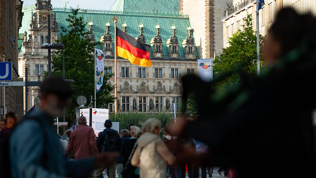 Vor dem Hamburger Rathaus weht eine große Deutschland-Fahne während Besucher über die Ländermeile auf der Mönckebergstraße laufen. Foto: Jonas Walzberg/dpa