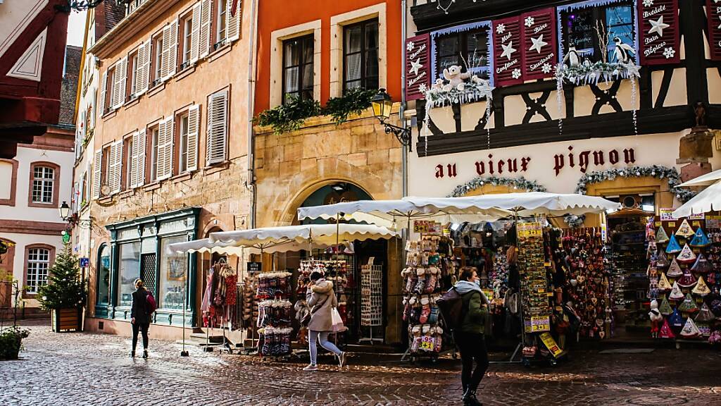 Menschen gehen in der Altstadt von Colmar an Geschäften vorbei. Im Elsass gilt ab Sonntag wegen des Coronavirus eine verschärfte abendliche Ausgangssperre. Foto: Philipp von Ditfurth/dpa