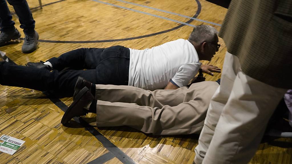 Anhänger des Präsidentschaftskandidaten Villavicencio gehen in Deckung in einer Turnhalle, als Schüsse zu hören sind. Villavicencio war am Mittwoch nach einer Wahlkampfveranstaltung erschossen worden. Foto: Uncredited/API/dpa