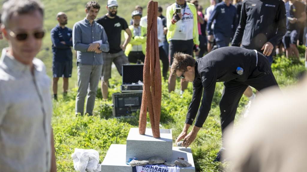Stefan Bissegger und mit ihm auch zahlreiche andere Radprofis legen einen Stein mit einer persönlichen Botschaft auf den Sockel der zu Ehren von Gino Mäder eingeweihten Skulptur
