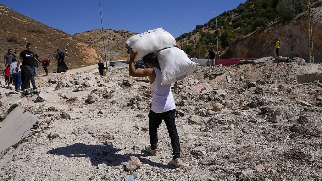 ARCHIV - Menschen tragen ihr Gepäck auf dem Weg nach Syrien durch einen Krater, der durch israelische Luftangriffe verursacht wurde. Foto: Hassan Ammar/AP/dpa