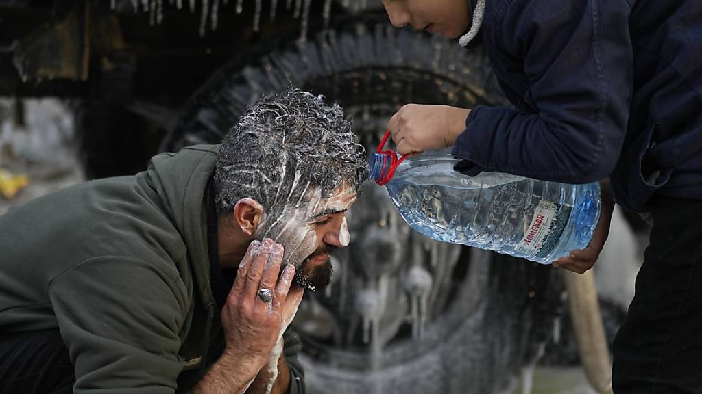 Ein Junge hilft einem Mann an der belarussisch-polnischen Grenze, sich den Kopf zu waschen. Foto: Pavel Golovkin/AP/dpa