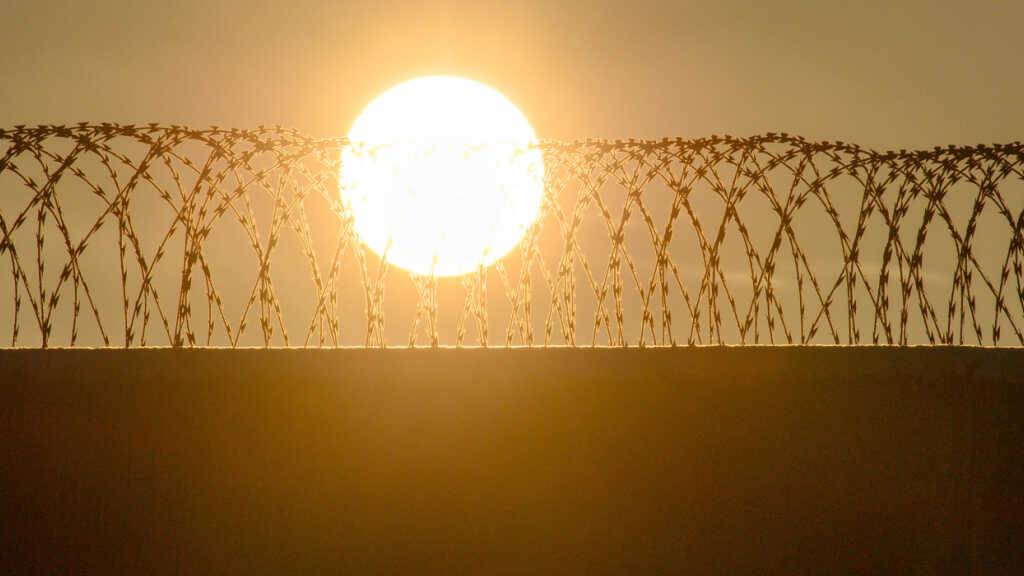 ARCHIV - Die Sonne geht über der drahtbewährten Mauer einer Justizvollzugsanstalt auf (Archivbild). Foto: Klaus-Dietmar Gabbert/dpa