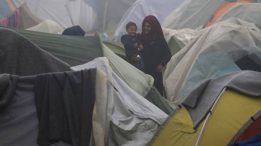 Eine Frau trägt vor einem Zelt im Flüchtlingslager von Idomeni im Norden Griechenlands ein Kleinkind auf den Armen.
