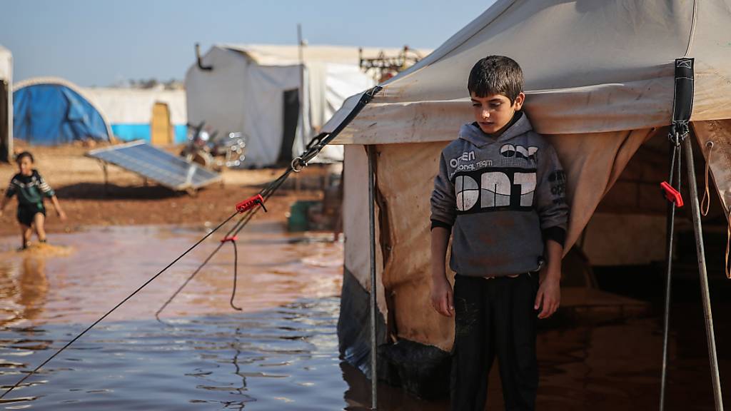 ARCHIV - Ein syrischer Junge steht in einem Flüchtlingslager, das vom Regen überflutet wurde, inmitten des schlammigen Wassers vor seinem Zelt. Foto: Anas Alkharboutli/dpa