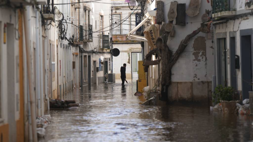 Ein Anwohner geht eine überflutete Straße entlang, nachdem der Fluss Sado nach heftigen Regenfällen in Alcácer do Sal, Südportugal, über die Ufer getreten ist. Foto: Ana Brigida/AP/dpa